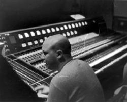 Black and white photo showing E.J. Gold sitting at sound studio mix board